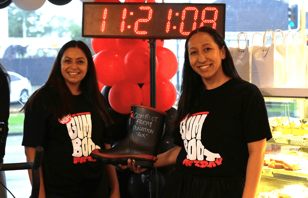 Two people in front of a digital timer board holding a gumboot for charity