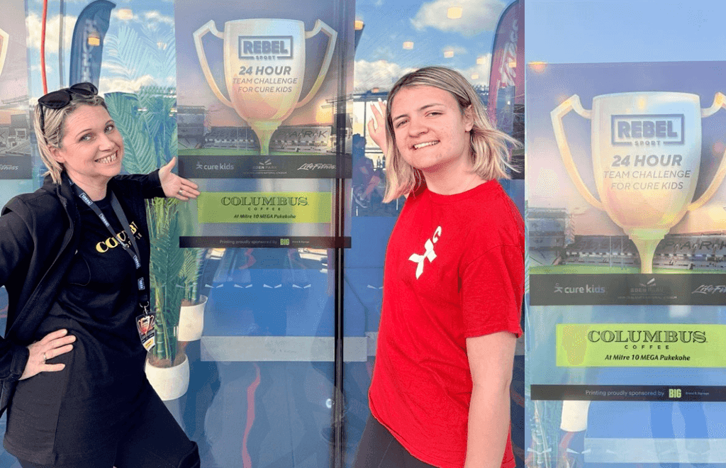 Two people posing for a photo in front of a poster