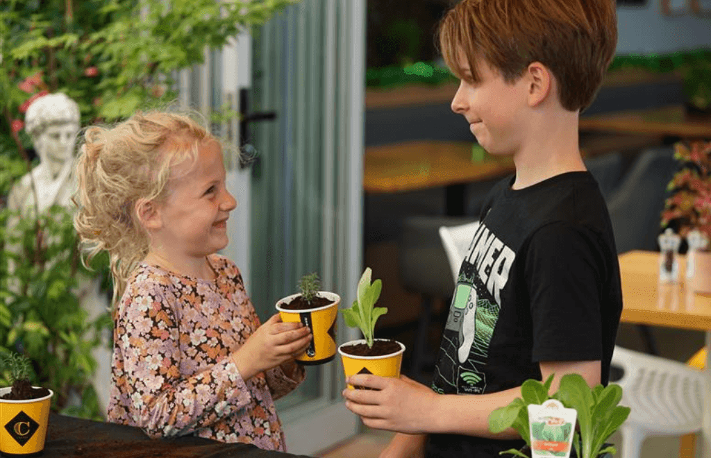 Two children looking at each other holding plant seedlings in a disposable coffee cup